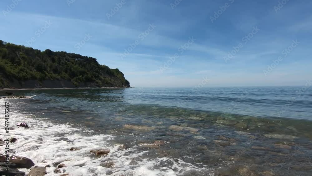 Slow motion view of seascape, reveal of sea waves gentle hitting pebble rocky beach. Moon Bay in Adriatic Sea, Slovenia. Wide shot, ascending Slow motion view of seascape, reveal of sea waves gentle hitting pebble rocky beach. Moon Bay in Adriatic Sea, Slovenia. Wide shot, ascending
