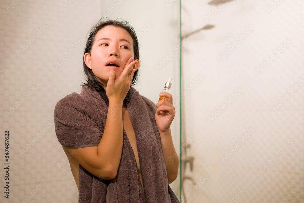 young beautiful and happy Asian Chinese woman applying serum facial skin care and face treatment in the bathroom enjoying morning routine in beauty concept young beautiful and happy Asian Chinese woman applying serum facial skin care and face treatment in the bathroom enjoying morning routine in beauty concept