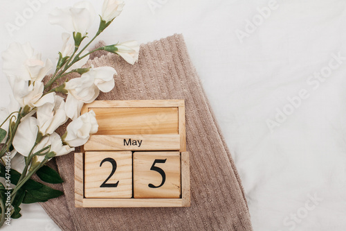 Flatlay gray terry towels on white bedding and a wooden calendar with the date of May 25th. Towels day. Copy space.
