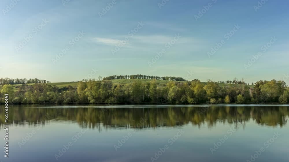Timelapse of calm lake surface with views of surrounding countryside full of hills stomas during a sunny day with movement white clouds in sky reflecting on the water surface Hustopece Czech Republic Timelapse of calm lake surface with views of surrounding countryside full of hills stomas during a sunny day with movement white clouds in sky reflecting on the water surface Hustopece Czech Republic