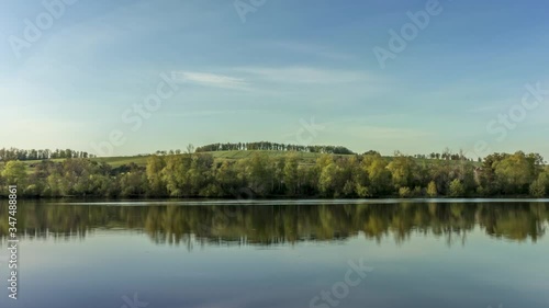 Timelapse of calm lake surface with views of surrounding countryside full of hills stomas during a sunny day with movement white clouds in sky reflecting on the water surface Hustopece Czech Republic photo