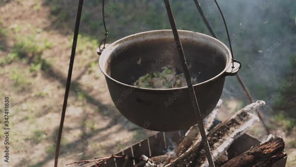 Food is prepared in a cauldron. The bowler boils at the stake, in the background is a flower country bed. Food is prepared in a cauldron. The bowler boils at the stake, in the background is a flower country bed.