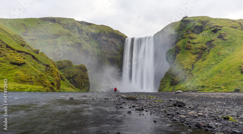 Man with red jacket hikes infront of the famous Skogarfoss waterfall in Iceland.