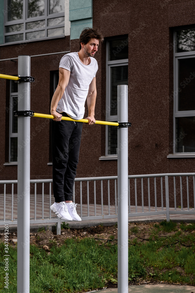 Man doing pull ups on the horizontal bar while training at evening outdoors, strong athlete in tracksuit doing exercise at street gym apparatus Man doing pull ups on the horizontal bar while training at evening outdoors, strong athlete in tracksuit doing exercise at street gym apparatus