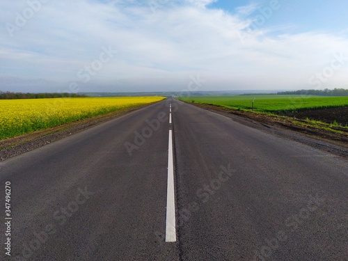 A smooth paved road with white lines marking between the field and the yellow rapeseed and the green field