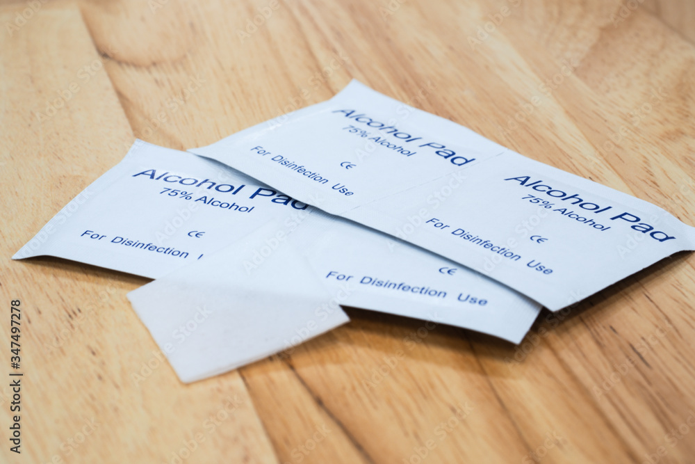 The close-up 1 unused alcohol pad over 4 alcohol pads in a package which are 75% alcohol with wood table background under warm light. The close-up 1 unused alcohol pad over 4 alcohol pads in a package which are 75% alcohol with wood table background under warm light.