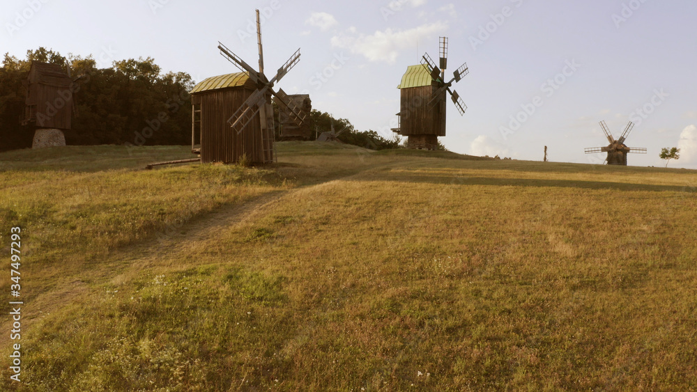 Fototapeta premium Old wooden windmills and big green meadow. Few little clouds on the rural sky.