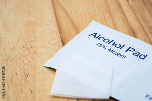 The close-up 1 unused alcohol pad over 2 alcohol pads in a package which are 75% alcohol with wood table background under warm light. photo