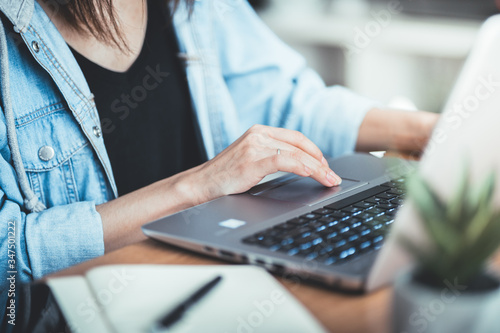 Cropped image of woman working at her office via laptop, young female manager using portable computer device while sitting at desk, flare light, work from home process concept