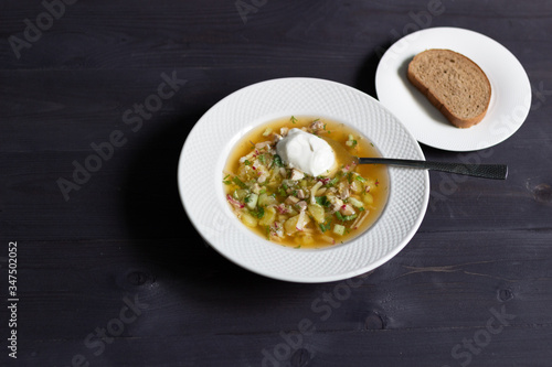 Plate of cold russian okroshka soup with sour cream and bread