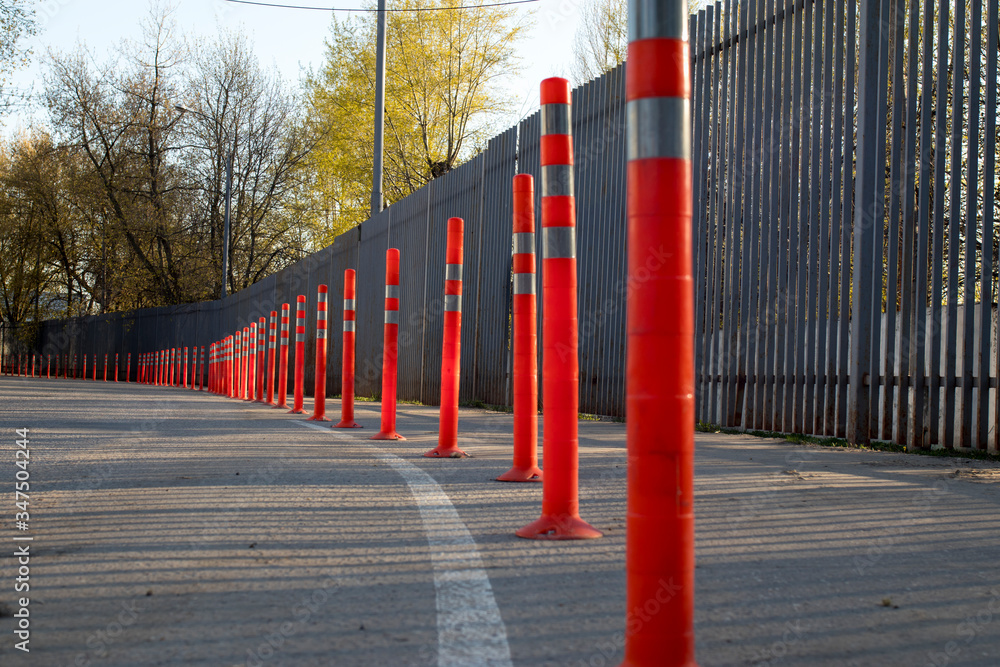 Red bounding posts along the road against a gray trellised fence.