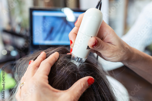 Foto Hairdresser examining client hair with a special apparatus for diagnostic hair and scalp in a hair shop