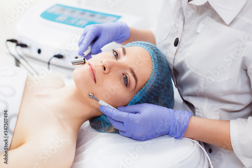 Cosmetology. Beautiful Woman At Spa Clinic Receiving Stimulating Electric Facial Treatment From Therapist. Closeup Of Young Female Face During Microcurrent Therapy.