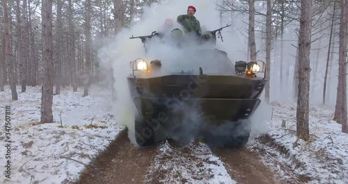 Winter. Smoke grenade. an APC with soldiers is approaching along a forest road photo