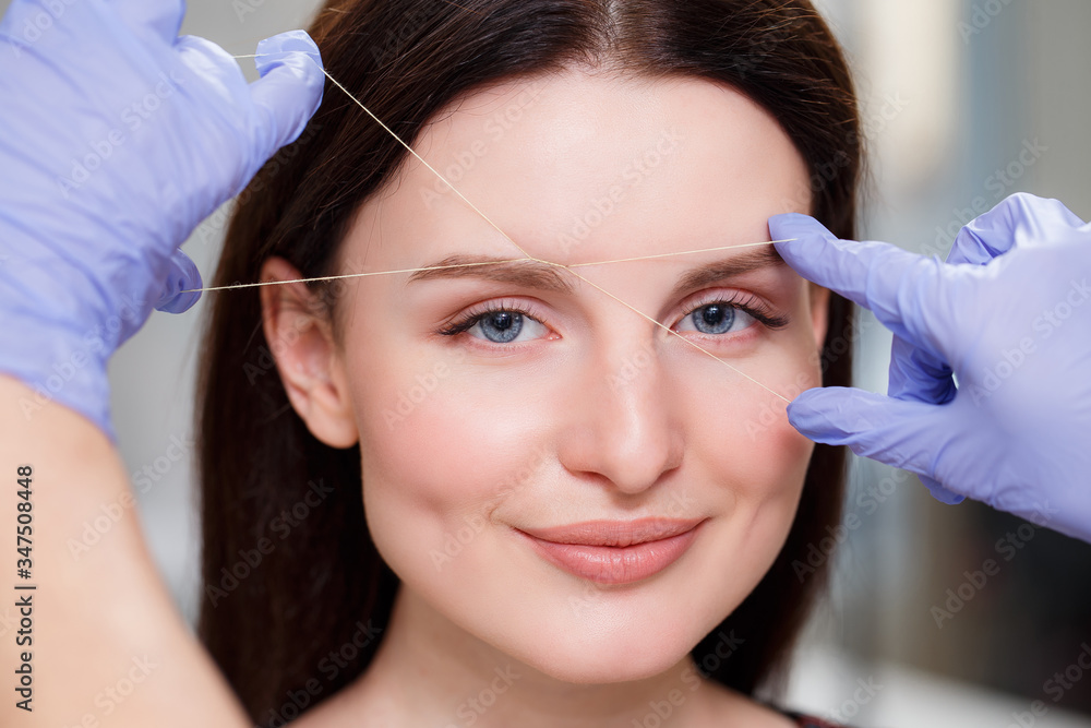 Cosmetologist plucks client eyebrows by thread. Close up Cosmetologist plucks client eyebrows by thread. Close up