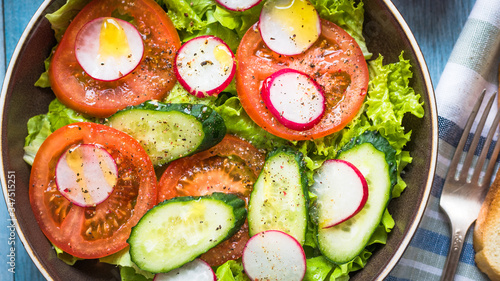 A very simple salad with fresh cucumbers, radishes, tomatoes and lettuce, olive oil and ground pepper - homemade summer European salad, top view