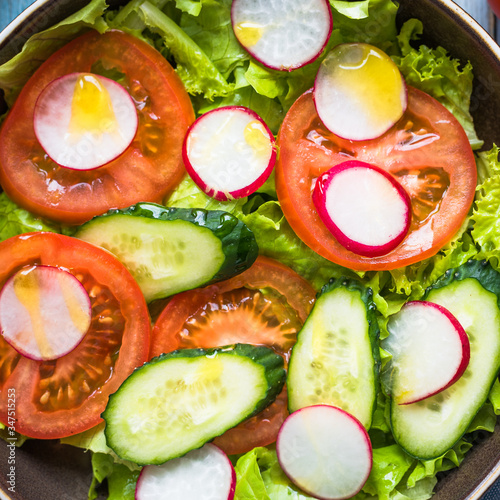 Simple vegetarian salad with fresh cucumbers, radishes, tomatoes and lettuce seasoned with olive oil close up