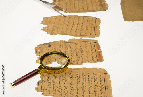 Book pages with an Arabic manuscript on a table with a light and a magnifying glass. Paleography, the study of ancient Arabic writing