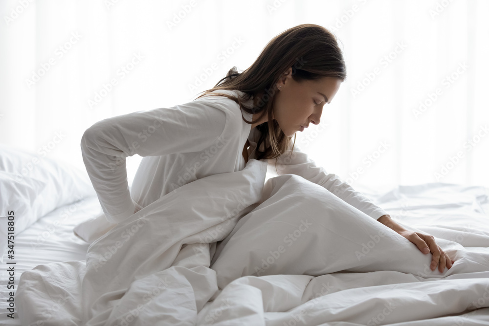 Side view of millennial woman woke up sitting in bed, unhealthy female woke  up feels severe lower back pain during period, pinched nerve discomfort in  vertebrae, herniated spinal disc symptoms concept foto