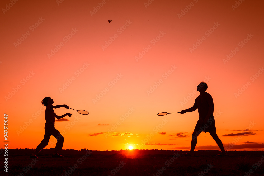 Father and son playing badminton in the evening, silhouettes of people exercising in nature, recreation, sport, lifestyle concept  