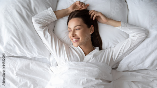 Woman in white pyjama lie under warm duvet feel rested renewed energy woke up looks away enjoy morning start day with smile, enough healthy sleep at home or hotel relish lazy weekend free time concept #347520011