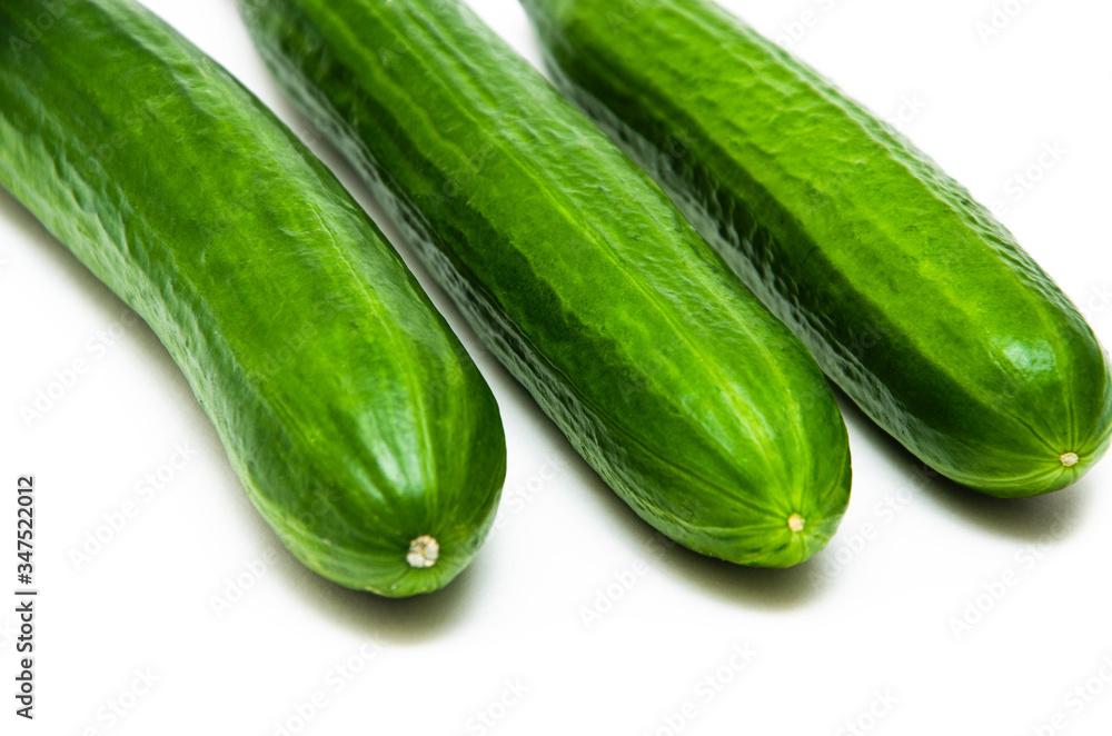 Three greenhouse green, smooth cucumbers on a white background nearby. Greenhouse cucumbers from above and in front. Cucumbers in macro, butt, tails of cucumbers Three greenhouse green, smooth cucumbers on a white background nearby. Greenhouse cucumbers from above and in front. Cucumbers in macro, butt, tails of cucumbers