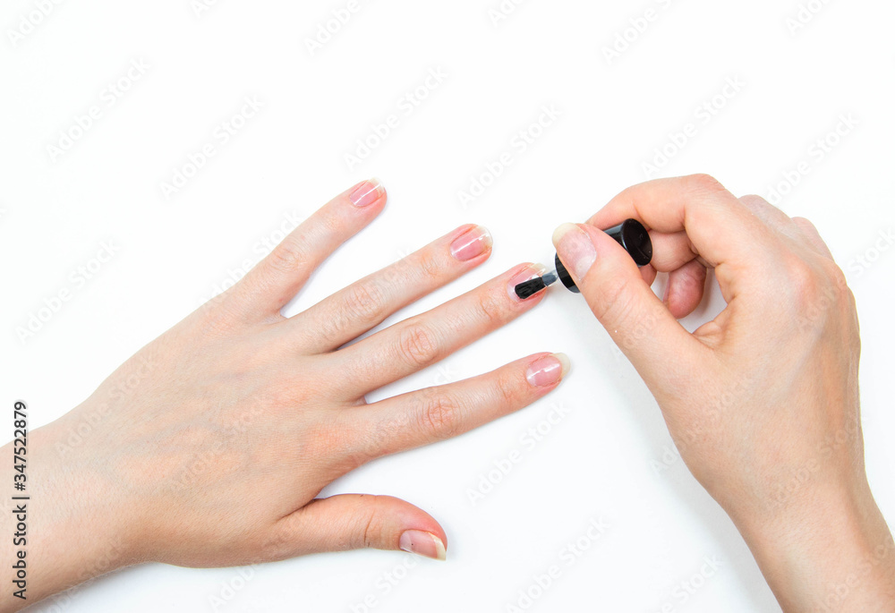 Manicure at home, during quarantine. Home manicure. The girl applies a transparent varnish, cuticle oil, nails on a white background with a brush on the nail. Macro Manicure at home, during quarantine. Home manicure. The girl applies a transparent varnish, cuticle oil, nails on a white background with a brush on the nail. Macro