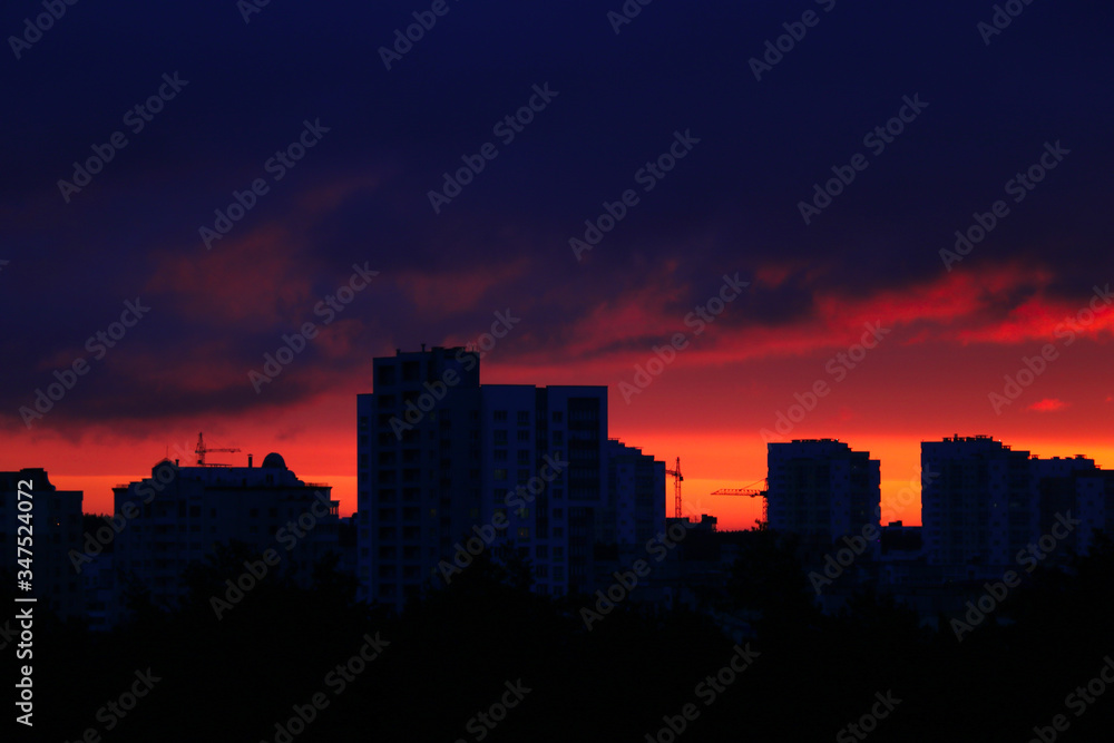 Silhouette of houses and construction cranes. Beautiful sunset in the city. Selective focus.