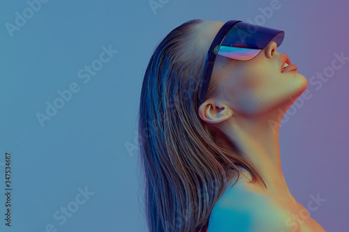 Foto Cool stylish girl with a fashionable hairstyle and stylish glasses with a large glass poses on a bright neon background
