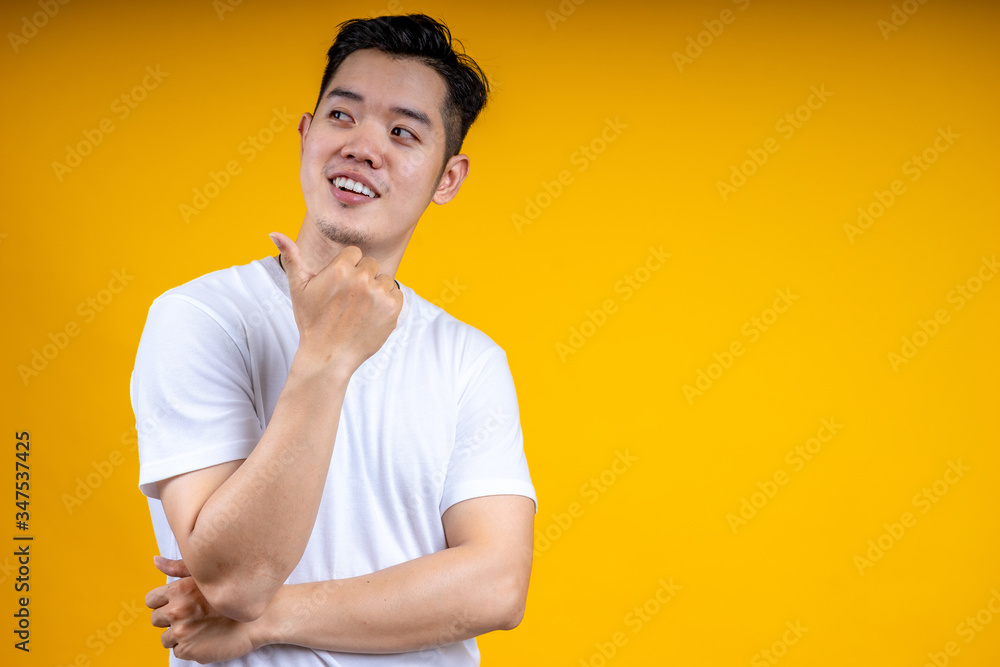 Image of cheerful young Asian man in basic clothing laughing looking aside isolated over yellow background Image of cheerful young Asian man in basic clothing laughing looking aside isolated over yellow background