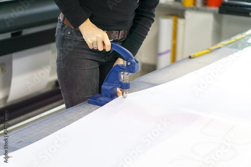 Woman assembles advertising banner with eyelet press photo