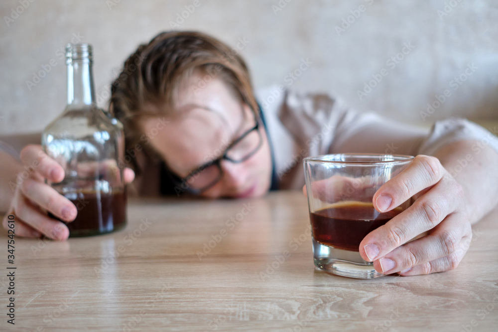 A man lies face on a table with a glass and a bottle of alcohol. A man lies face on a table with a glass and a bottle of alcohol.