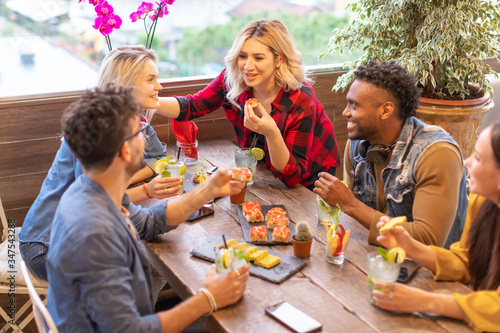 Multiracial group of young millennials friends talking and dining together - students party at rooftop cafe