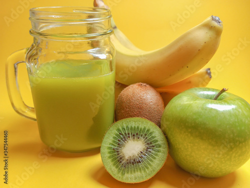 Green healthy smoothie in glass jar: banana, kiwi, green apple. Healthy drink on yellow background.