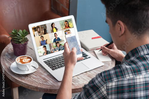 A man use laptop with screen of video conference meeting  with 9 other people and taking notes, work from home comceptual photo