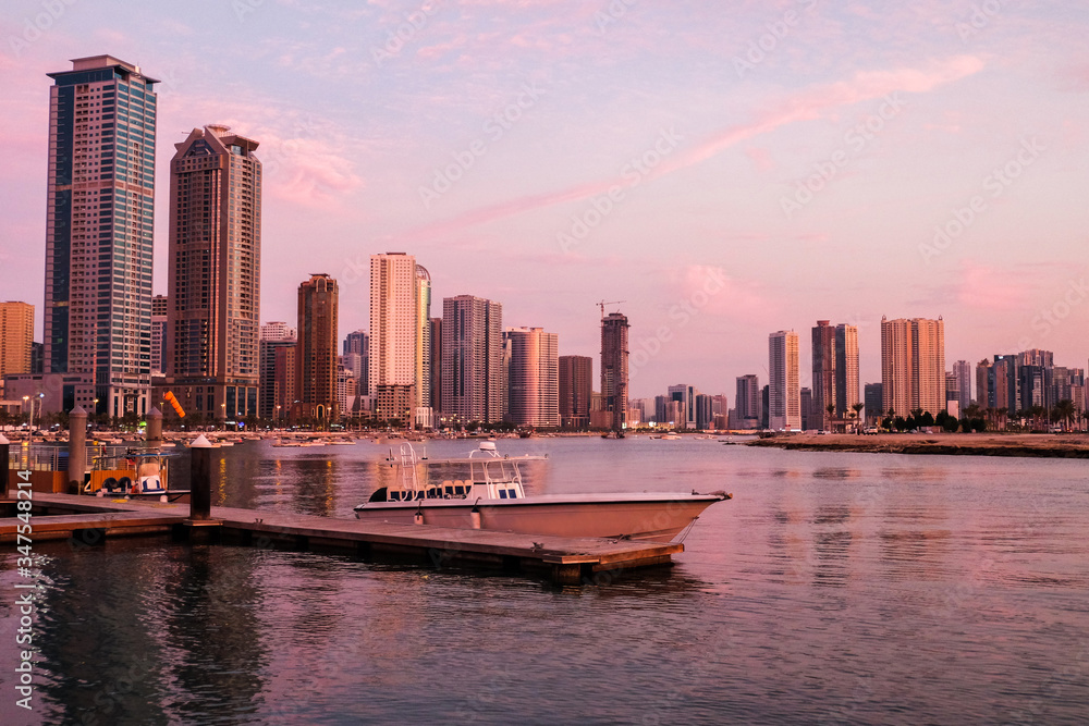 Sunset in the UAE Emirate of Sharjah-yacht, boat on the background of skyscrapers. Background color with gradient and grain, sound effect. Yacht club at sunset in megapolis
