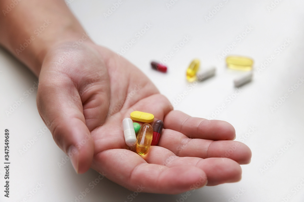 Top view of Colorful pills, capsule medicines and glass of water in man's hands. Treating COVID-19 at home on the doctor's recommendations. Top view of Colorful pills, capsule medicines and glass of water in man's hands. Treating COVID-19 at home on the doctor's recommendations.