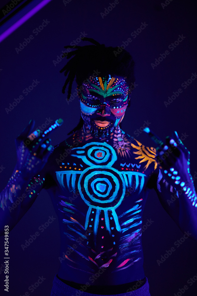 cool african boy with fluorescent make-up showing fuck gesture at camera, fearless man isolated in dark studio, luminescent paint glows in neon lights cool african boy with fluorescent make-up showing fuck gesture at camera, fearless man isolated in dark studio, luminescent paint glows in neon lights