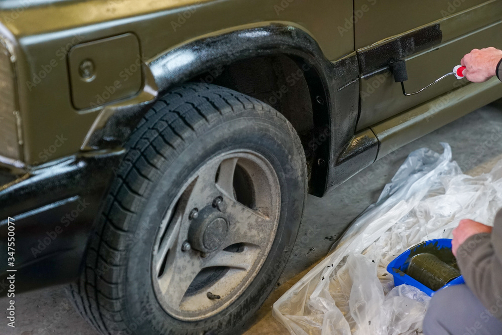 close up of a man painting an army jeep and adding black trim