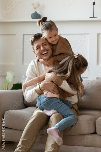 Quadro su tela Funny little girls hugging cuddling smiling laughing father sitting on comfortab