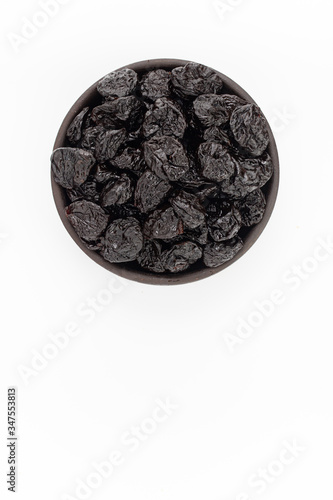 Dried plumps in round bowl on white background, top view