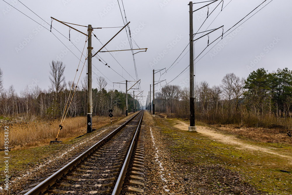 Railroad track and electrical power line in the forest at autumn