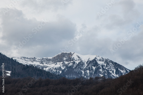 A snowy mountain range in a cloudy sky and dark forest. Winter cloud landscape of mountains. Mountains Sochi, Russia