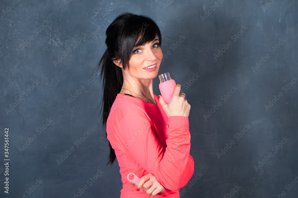 Trendy beautiful girl, brunette in bright sports clothes looks into the camera, smiles, holding a bottle of water. Ready to start training. The concept of sports, fitness, space for text Trendy beautiful girl, brunette in bright sports clothes looks into the camera, smiles, holding a bottle of water. Ready to start training. The concept of sports, fitness, space for text
