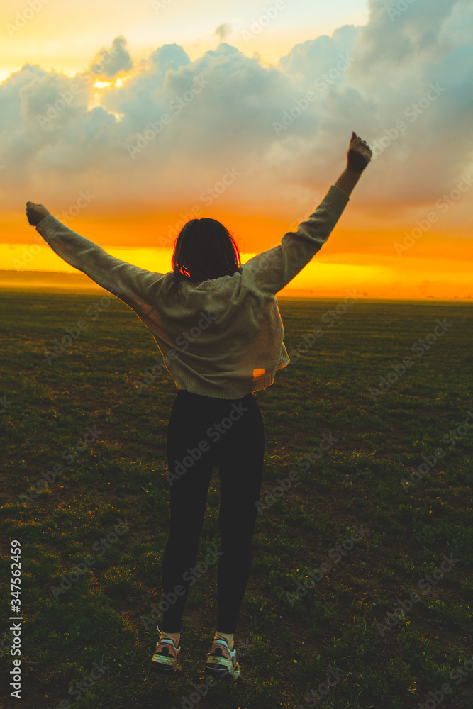 Young woman jumping in green field on the sunset. Beautiful girl on the nature - obrazy, fototapety, plakaty 