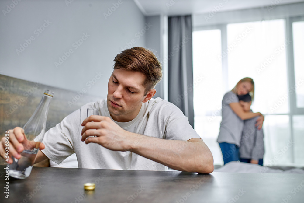 Fototapeta premium wife and son want a normal, prosperous family without an alcoholic dad, unhappy woman with son stand hugging in the background. man doesn't even pay attention to them