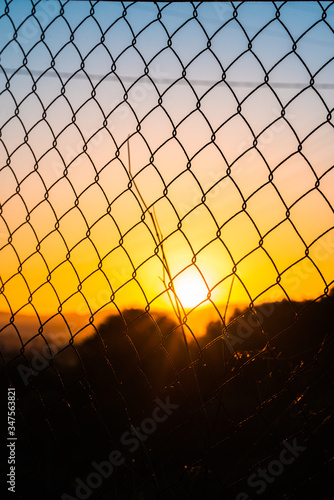 sunrise behind a metal fence with an electricity tower in the background.