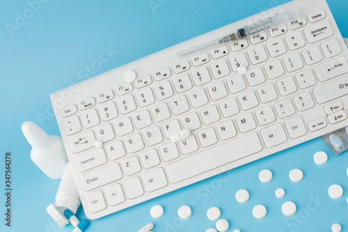Shopping cart toy with medicaments and Keyboard. Pills, blister packs, medical bottles, thermometer, protective mask on a blue background. Top view with place for your text