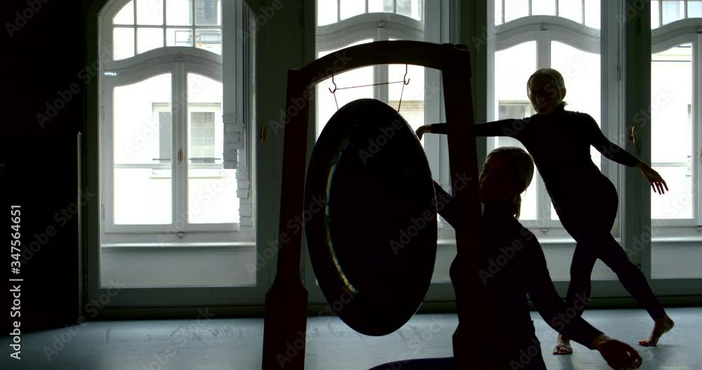 two black female silhouettes against arched Windows. one woman sits in front of the Gong and beats it. the other holds out her hands. the camera zooms in two black female silhouettes against arched Windows. one woman sits in front of the Gong and beats it. the other holds out her hands. the camera zooms in