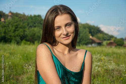 Beautiful young woman in a green dress is smiling at the rural landscape background